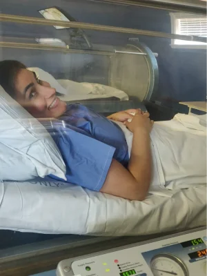 Dr Zeest Khan reclining in a medical bed, wearing a mask.